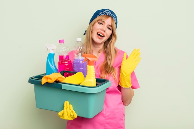 Redhead bella donna sorridente felicemente agitando la mano dandoti il benvenuto e salutandoti pulizie e prodotti puliti