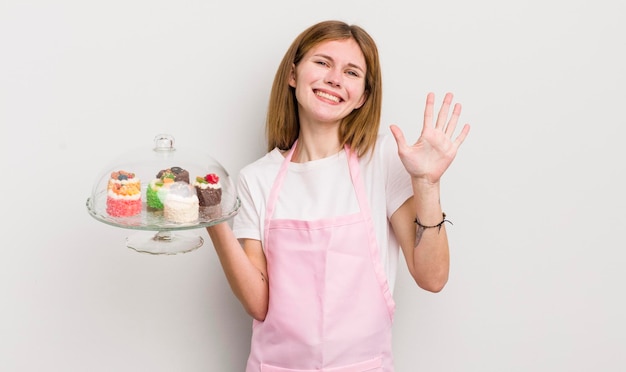 Redhead bella ragazza sorridente e dall'aspetto amichevole che mostra il concetto di torte fatte in casa numero cinque