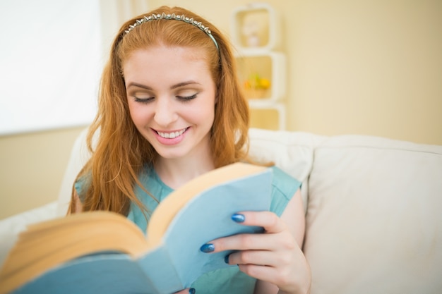 Redhead felice che legge un libro sul divano