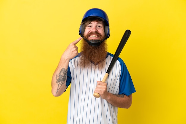Redhead giocatore di baseball uomo con casco e pipistrello isolato su sfondo giallo dando un pollice in alto gesto