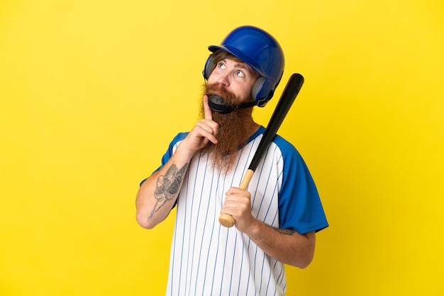 Redhead giocatore di baseball uomo con casco e pipistrello isolato su sfondo giallo guardando in alto mentre sorride