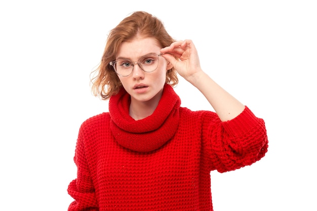 Redhead giovane donna con gli occhiali che strizza gli occhi mentre guarda la fotocamera isolata su sfondo bianco Concetto di problemi di visione