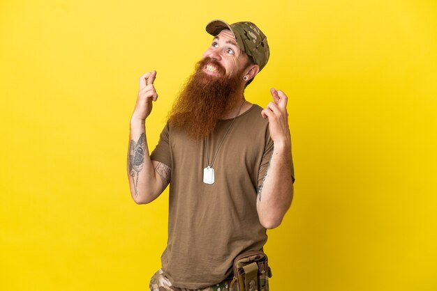 Redhead militare con dog tag isolato su sfondo giallo con le dita incrociate