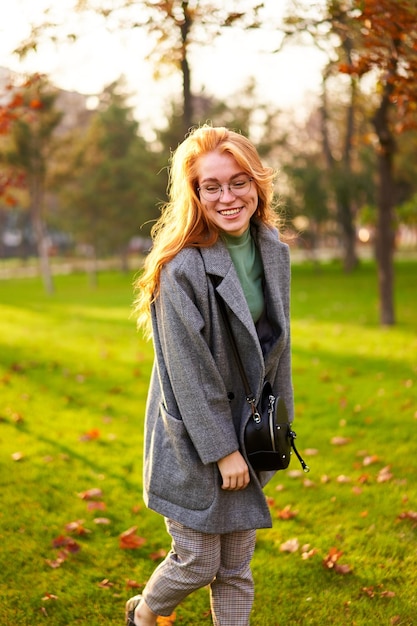 Redhead sorridente bella donna che cammina nel parco in una giornata di sole autunnale eleganti pose femminili in elegante