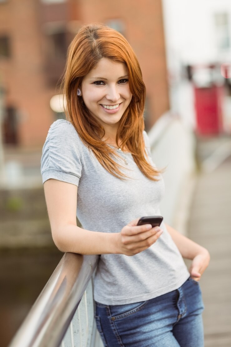 Foto redhead sorridente con il suo telefono cellulare che manda un sms ad un messaggio