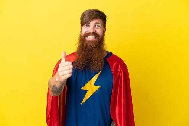 Redhead Super Hero uomo isolato su sfondo giallo che stringe la mano per aver chiuso un buon affare