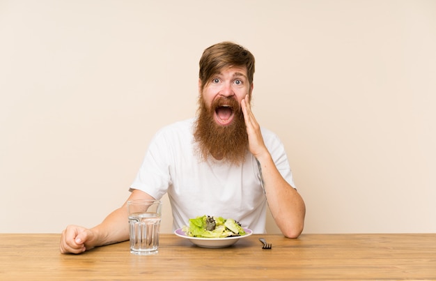 Redhead uomo con la barba lunga e con insalata con sorpresa e scioccata espressione facciale