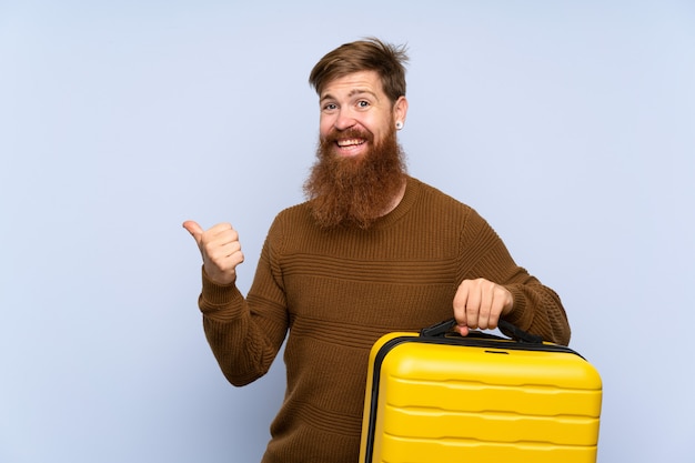 Redhead uomo con la barba lunga in possesso di una valigia che punta verso il lato per presentare un prodotto