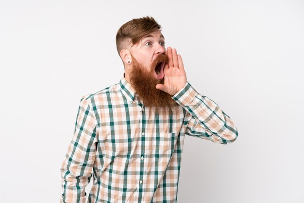 Redhead uomo con la barba lunga sul muro bianco isolato gridando con la bocca spalancata sul lato
