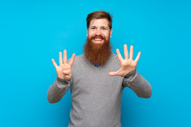 Redhead uomo con la barba lunga sul muro blu contando nove con le dita