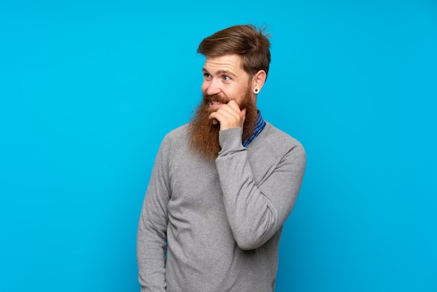 Redhead uomo con la barba lunga sul muro blu, guardando al lato