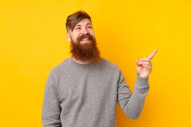 Redhead uomo con la barba lunga sul muro giallo che punta il dito verso il lato