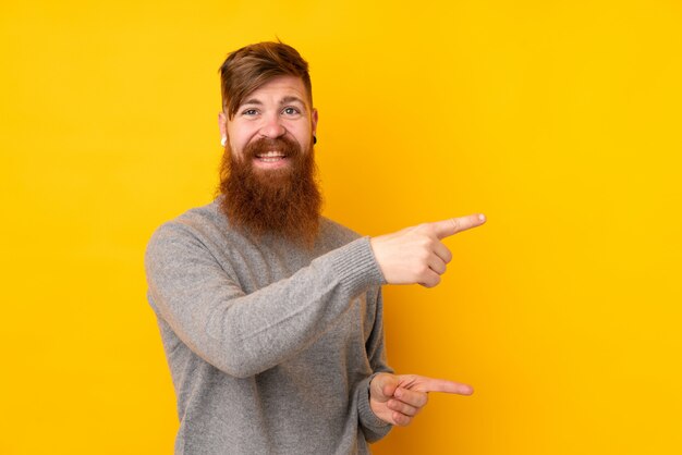 Redhead uomo con la barba lunga sul muro giallo isolato che punta il dito verso il lato e che presenta un prodotto