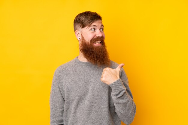 Redhead uomo con la barba lunga sul muro giallo isolato che punta verso il lato per presentare un prodotto