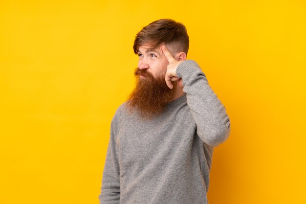 Redhead uomo con la barba lunga sul muro giallo isolato facendo il gesto della follia mettendo il dito sulla testa