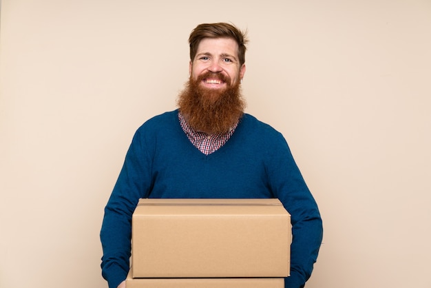 Redhead uomo con la barba lunga sul muro isolato in possesso di una scatola per spostarlo in un altro sito