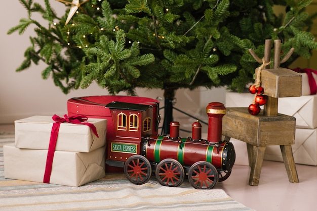 Regali di Natale, locomotiva giocattolo e cervi di legno giocano sotto l'albero di Natale