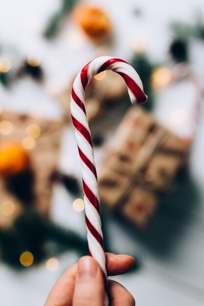 Regali di Natale, mano tiene lecca-lecca, mandarino su fondo di legno bianco. Foto di alta qualità