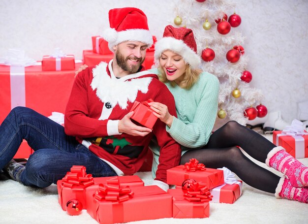 Regali di Natale preparati in famiglia. Coppia di innamorati coccola sorridendo mentre disimballa il fondo dell'albero di Natale del regalo. Le coppie innamorate felici godono della celebrazione delle vacanze di Natale con i regali. Regalo all'amato.