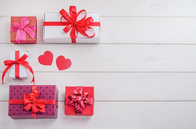 Regali, sfondi per San Valentino, festa della mamma. Contenitori di regalo multicolori con nastri rossi e cuori su un fondo di legno bianco con lo spazio della copia. Saldi festivi, congratulazioni.