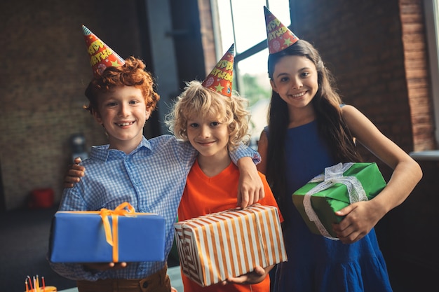 Regali. Tre amici in cappelli di compleanno che tengono i regali