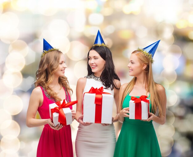 regali, vacanze, persone e concetto di celebrazione - donne sorridenti in cappellini da festa con scatole regalo su sfondo di luci