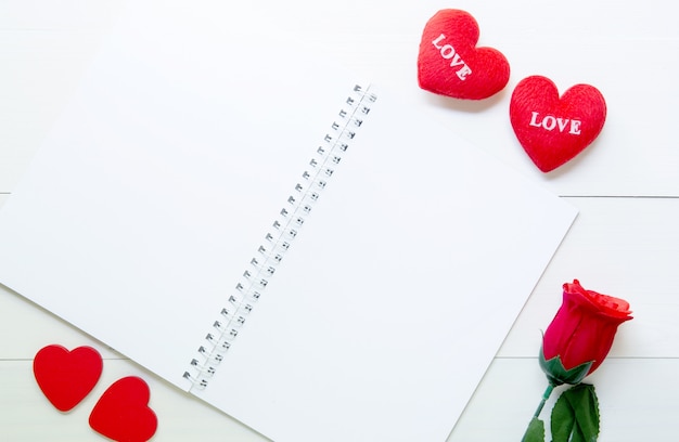 Regalo attuale con fiore rosa rossa e forma di cuore e notebook sul tavolo di legno