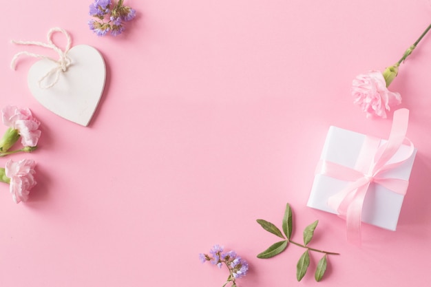 Regalo, cuore bianco in legno e fiori su sfondo rosa