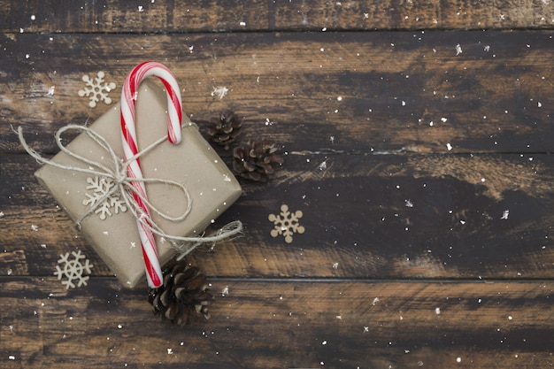 Regalo di Natale avvolto in carta artigianale con bastoncino di zucchero sul tavolo di legno marrone.