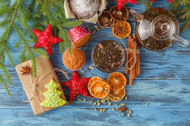 Regalo di natale avvolto in una carta del mestiere e in un nastro controllato con i biscotti del pan di zenzero e bastoncini di cannella su una tavola di legno con il ramoscello dell'albero di Natale.