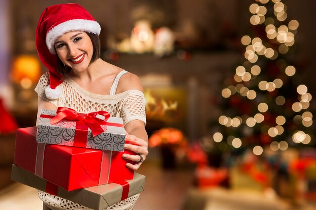 Regalo di Natale della tenuta del ritratto della donna isolata cappello della Santa di Natale. Sorridente ragazza felice su sfondo natalizio