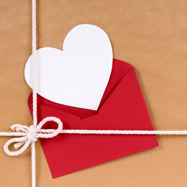 Regalo di San Valentino con la carta bianca di forma del cuore, busta rossa, fondo del pacchetto del pacchetto della carta marrone