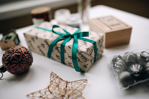 Regalo dipinto avvolto con nastro verde da vicino sul tavolo bianco con giocattoli di Natale