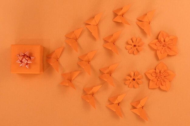 Regalo farfalla origami arancione e fiori di carta su sfondo arancione