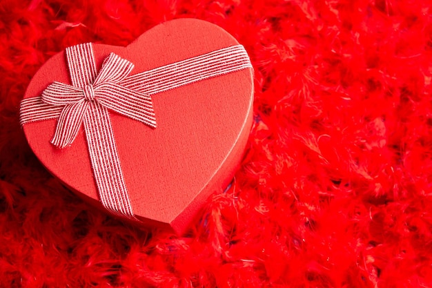 Regalo in scatola a forma di cuore posto su sfondo di piume rosse Il giorno di San Valentino o il concetto di data romantica Vista dall'alto con spazio per la copia