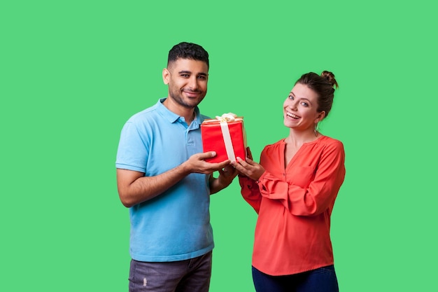 Regalo per la famiglia Ritratto di coppia felice in abbigliamento casual in piedi che tiene scatola con presente e guardando la fotocamera insieme godendo la sorpresa delle vacanze isolata su sfondo verde studio indoor girato