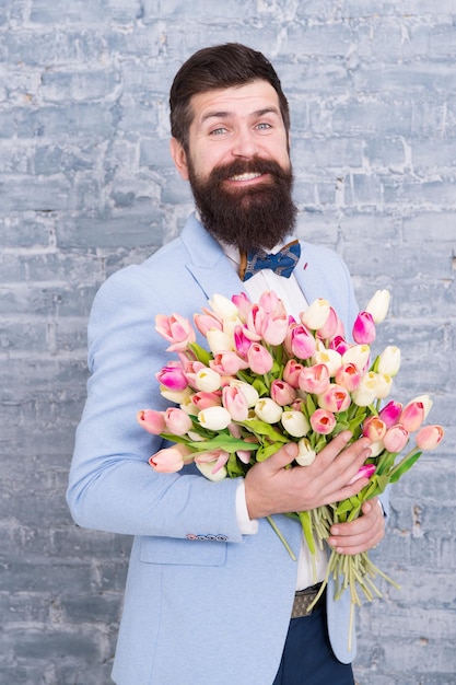 Regalo romantico. Macho si prepara per un appuntamento romantico. Tulipani per l'innamorato. L'uomo ben curato indossa il papillon blu dello smoking con un bouquet di fiori. Aspettando la sua ragazza. Uomo romantico con fiori.