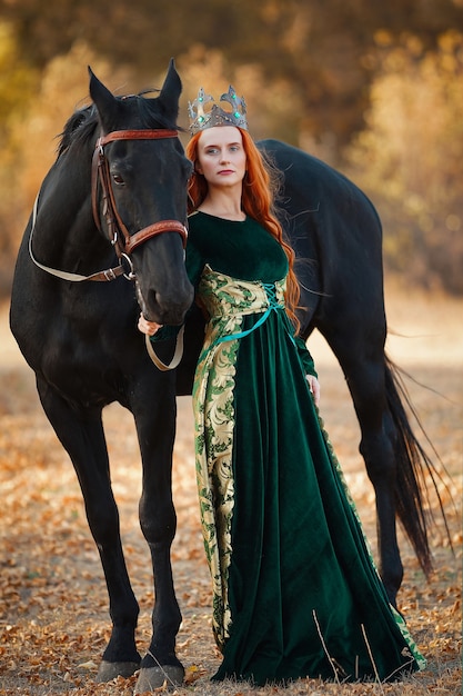 Regina con i capelli rossi in un abito verde con una corona e vicino a un cavallo