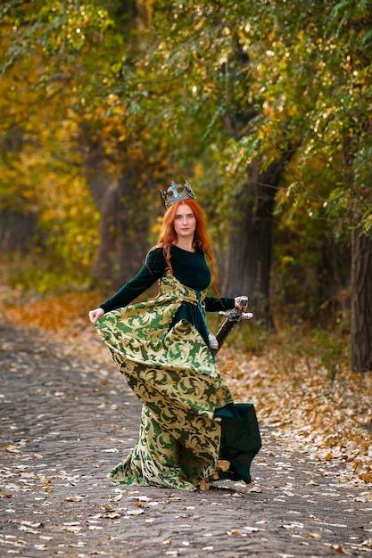 Regina con i capelli rossi in un abito verde con una corona nella foresta