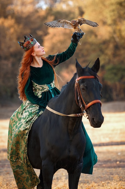 Regina con i capelli rossi in un abito verde e corona con un cavallo e un uccello