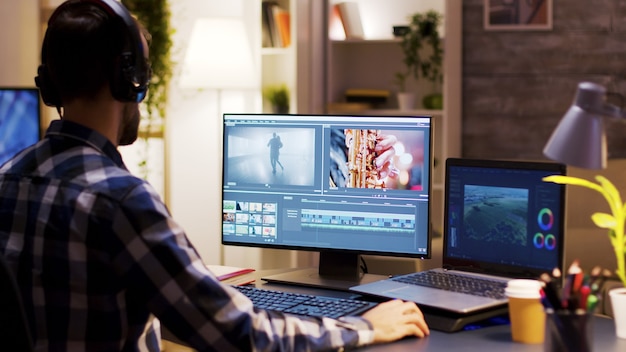 Regista che punta al monitor in ufficio a casa mentre lavora alla post-produzione per un film. Editor video che indossa le cuffie.