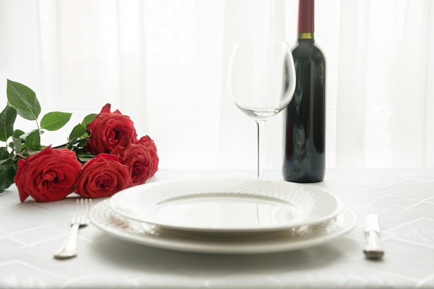 Regolazione del posto di giorno di San Valentino con rose rosse bouquet e vino.