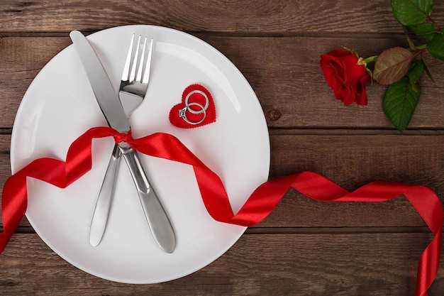 Regolazione della tabella di giorno di biglietti di S. Valentino con il nastro rosso dell'anello del cuore del coltello della forcella del piatto e la priorità bassa della rosa