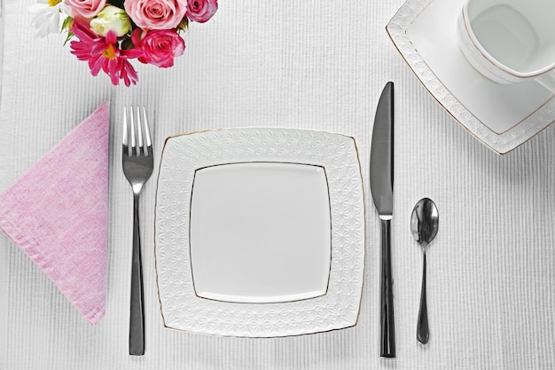 Regolazione della tavola con piatti posate e fiori su sfondo bianco