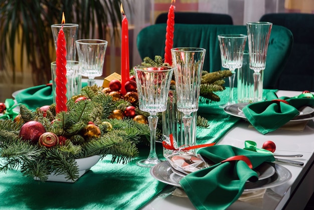 Regolazione della tavola di Natale con candele, bicchieri e rami di abete. Tavola festiva nei colori rosso e verde.