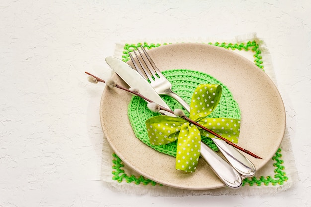 Regolazione della tavola di Pasqua sul fondo bianco strutturato del mastice. Modello di carta vacanze di primavera. Posate, tovaglioli ricamati, fiocco, sigilli di salice