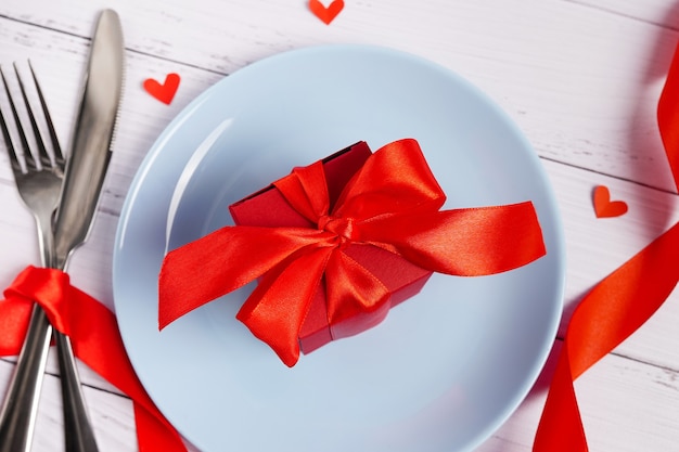 Regolazione festiva della tavola per San Valentino con confezione regalo rossa, forchetta, coltello e cuori