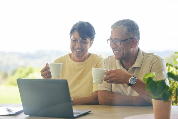 Relax al computer portatile e coppia di anziani che trasmettono in streaming uno spettacolo comico online su Internet o da un servizio in abbonamento sul Web Caffè mattutino e anziani felici insieme in una casa che guardano un film