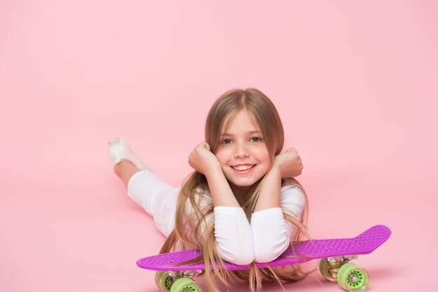 Relax e divertimento Infanzia felice Kid ragazza relax magra penny board Moderno hobby giovanile Concetto di svago da ragazza Ragazza faccia felice giaceva su penny board sfondo rosa Ragazze originariamente progettate skateboard