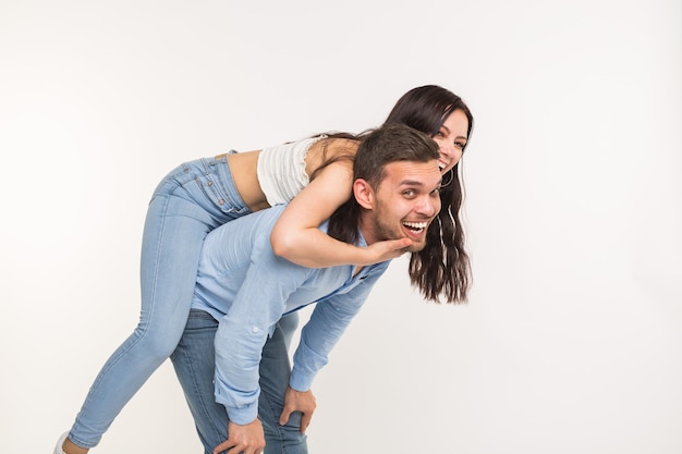 Relazione e concetto di divertimento - Uomo felice che trasporta la sua ragazza sulla parte posteriore sulla superficie bianca